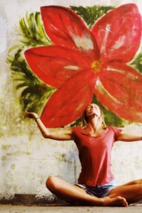 Kelley Doyle seated with arms spread, with a large red flower painted flower behind her